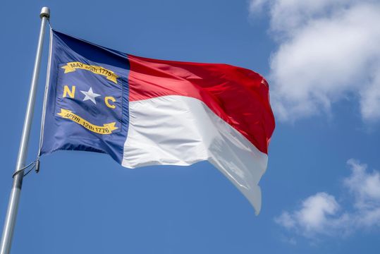 North Carolina state flag waving against a blue sky with clouds