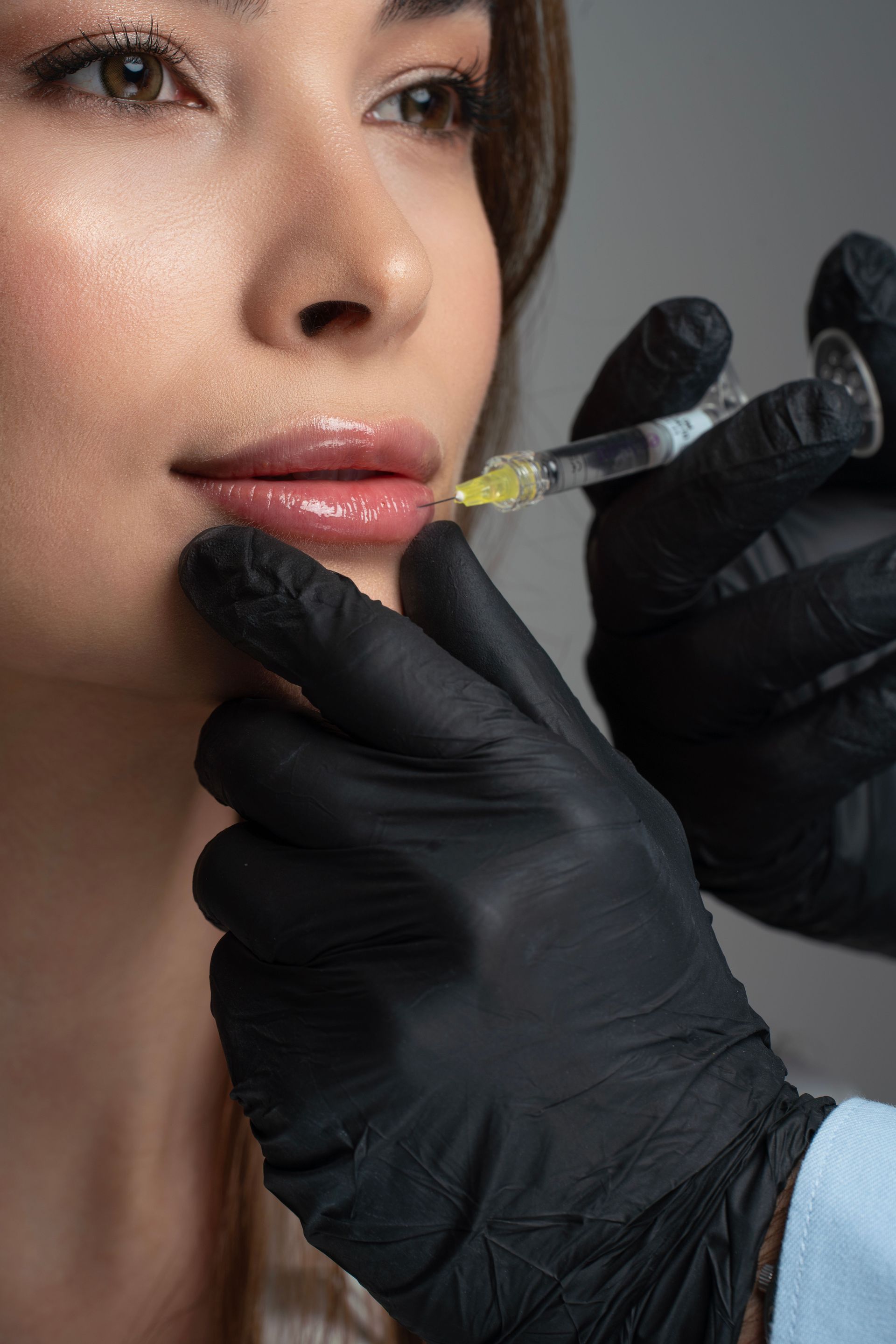 Practitioner in gloves injecting filler into a client's lips