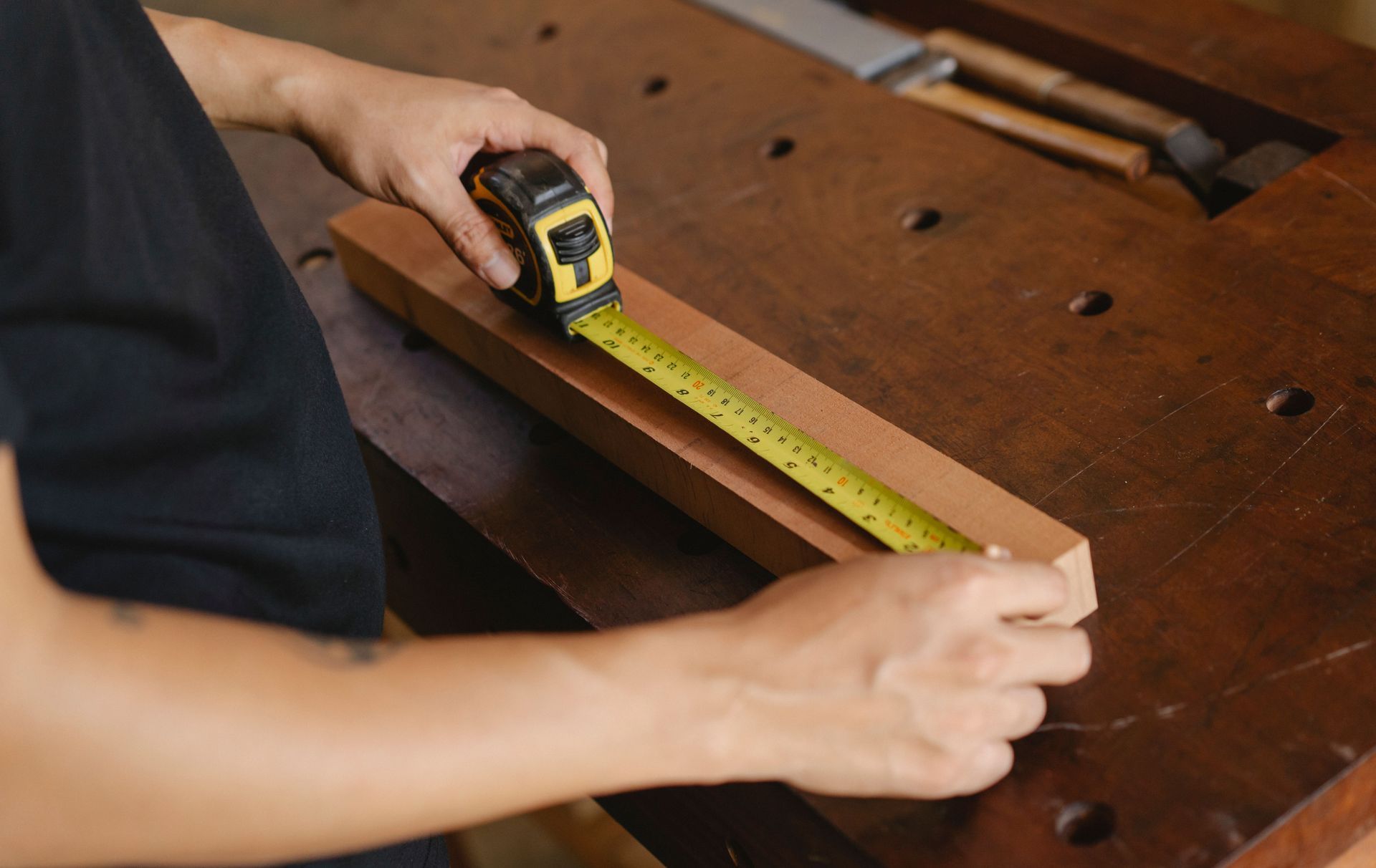 Hands measuring a timber board with a tape measure