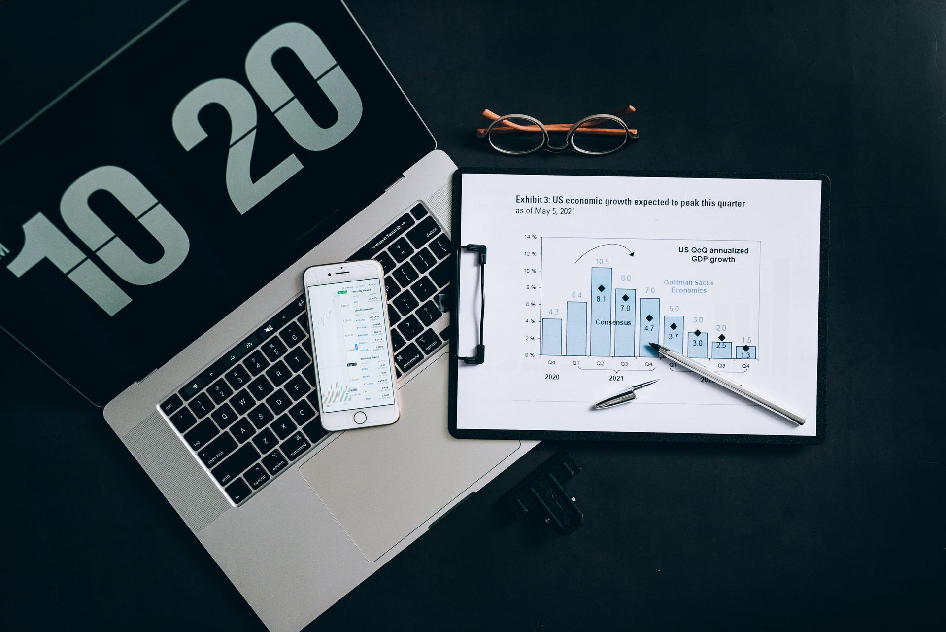 Printed charts, a phone and a laptop on a dark desk