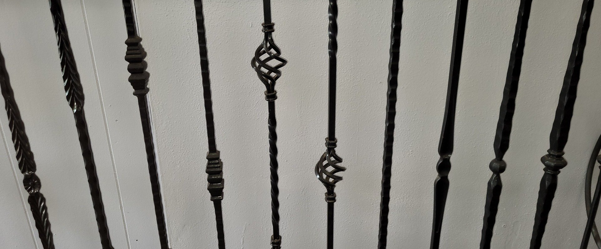 Black wrought-iron stair railing with decorative vertical balusters against a light wall.