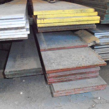 Stacks of flat metal sheets in white, yellow, gray, and red, piled on a floor in a storage area