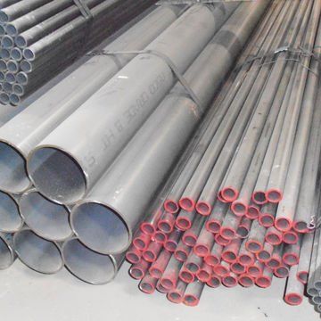 Stacks of silver metal pipes and red-capped tubes arranged in a warehouse.