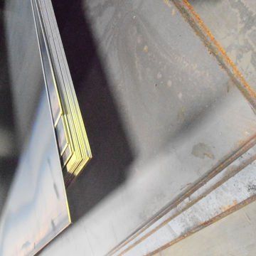 Close-up of a metal structure with rusted seams and a yellow-and-silver edge in an industrial setting