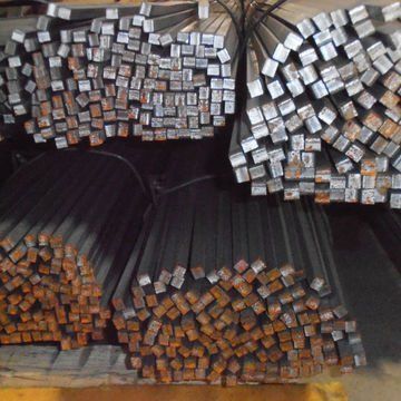 Stacks of metal rods with square ends, bundled in rows in a warehouse or storage yard.