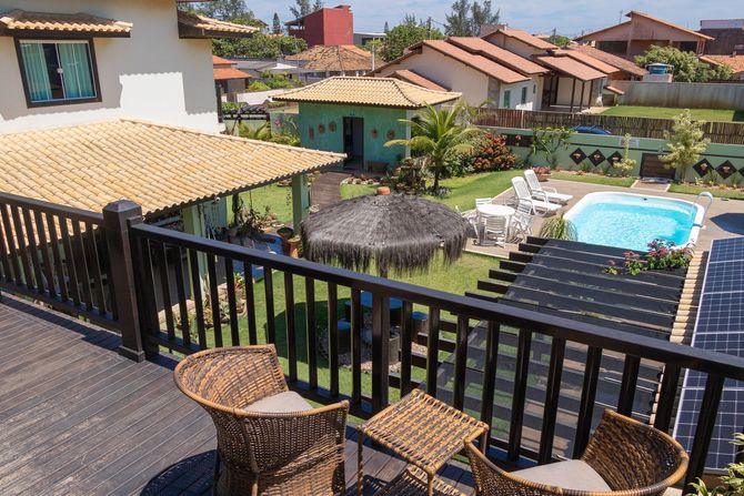 Pátio do resort com piscina, guarda-sóis de palha, espreguiçadeiras e vilas com telhado de telha, além de um terraço.