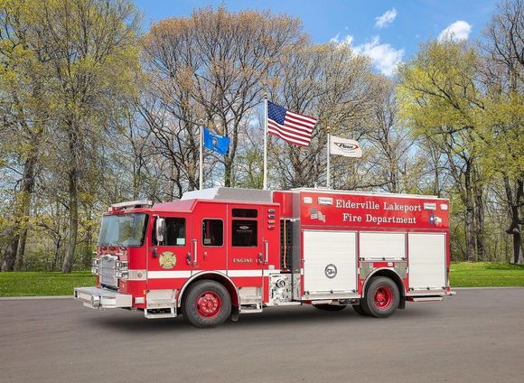 A red fire truck in front of some flags with trees in the background.