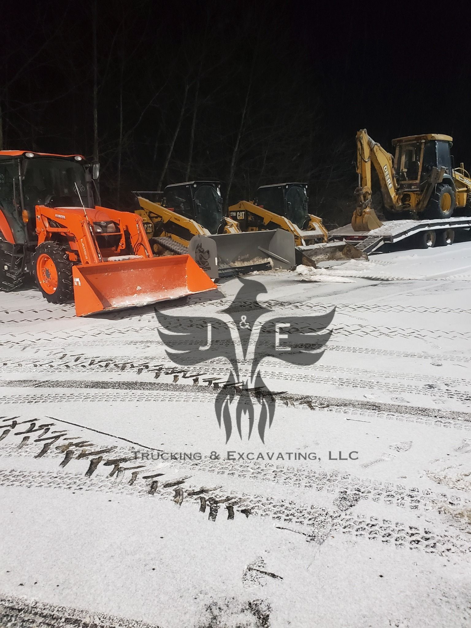 Snow-covered construction site with orange and yellow excavators and loaders at night