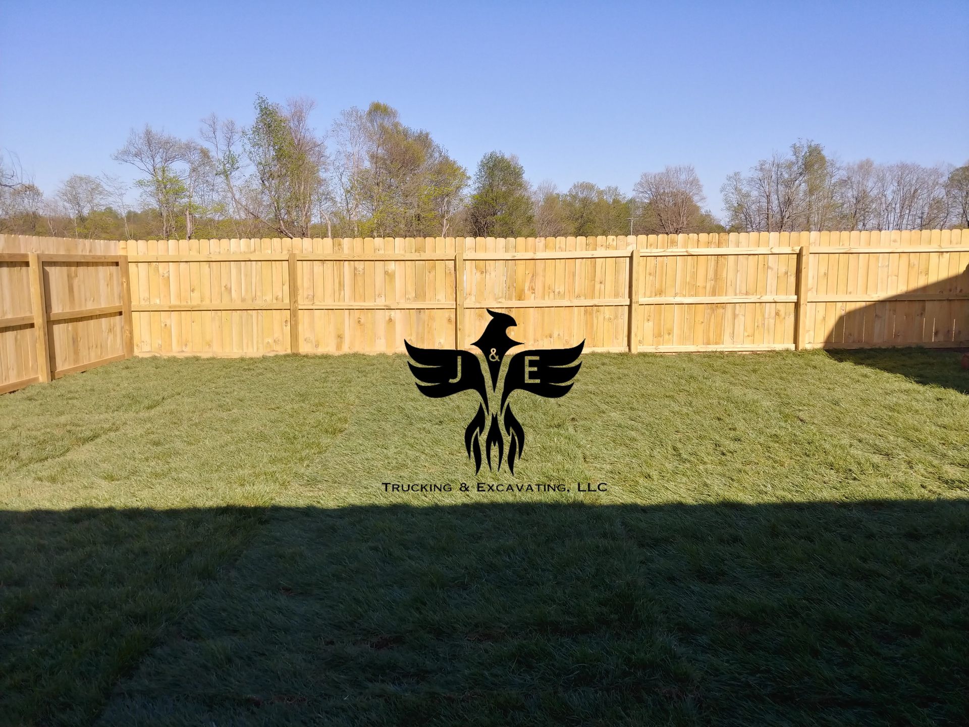 Backyard with wooden fence and green grass, featuring a black eagle emblem in the center.