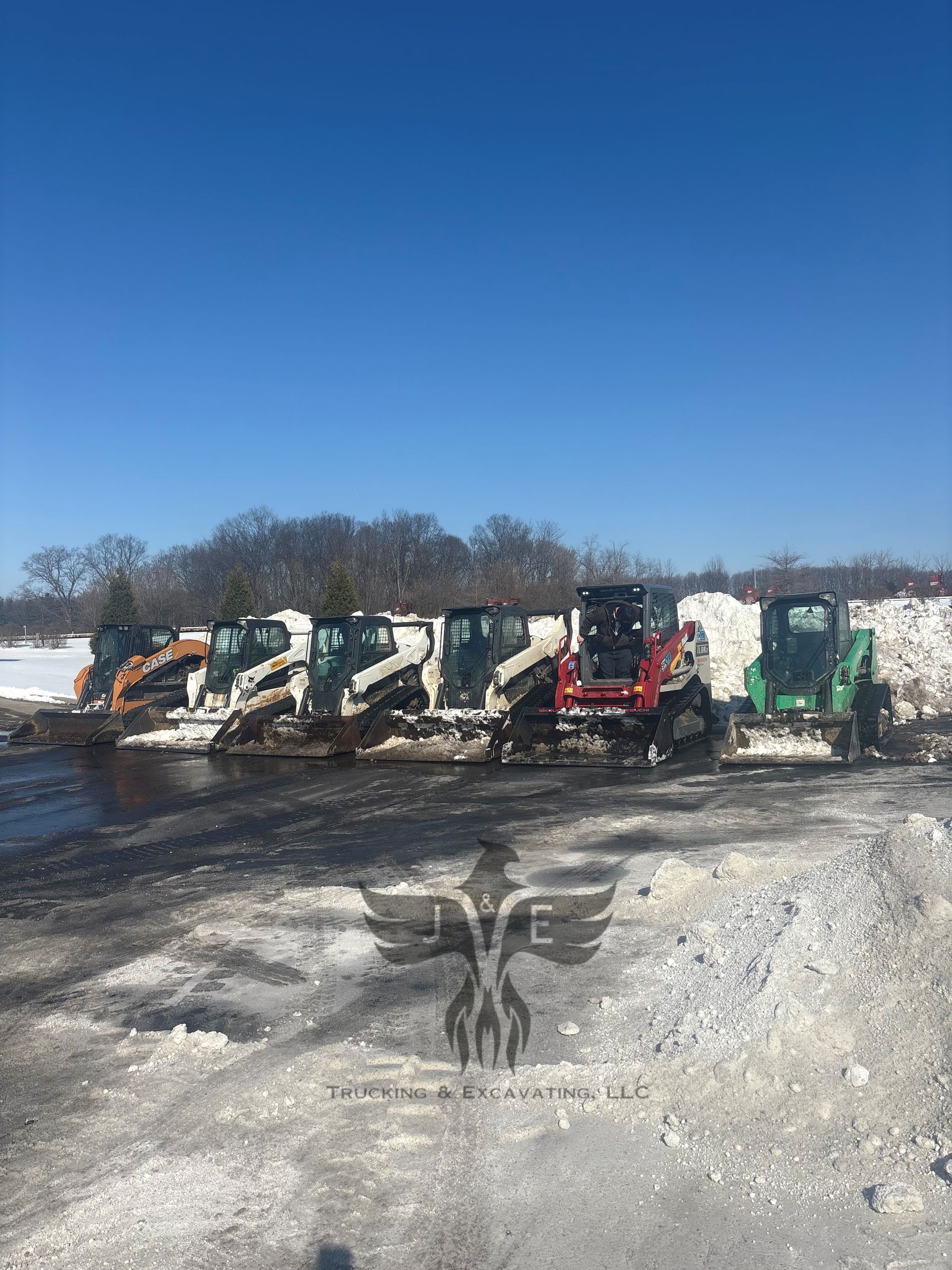 Row of excavators and dump trucks parked on a snowy construction site under a clear blue sky