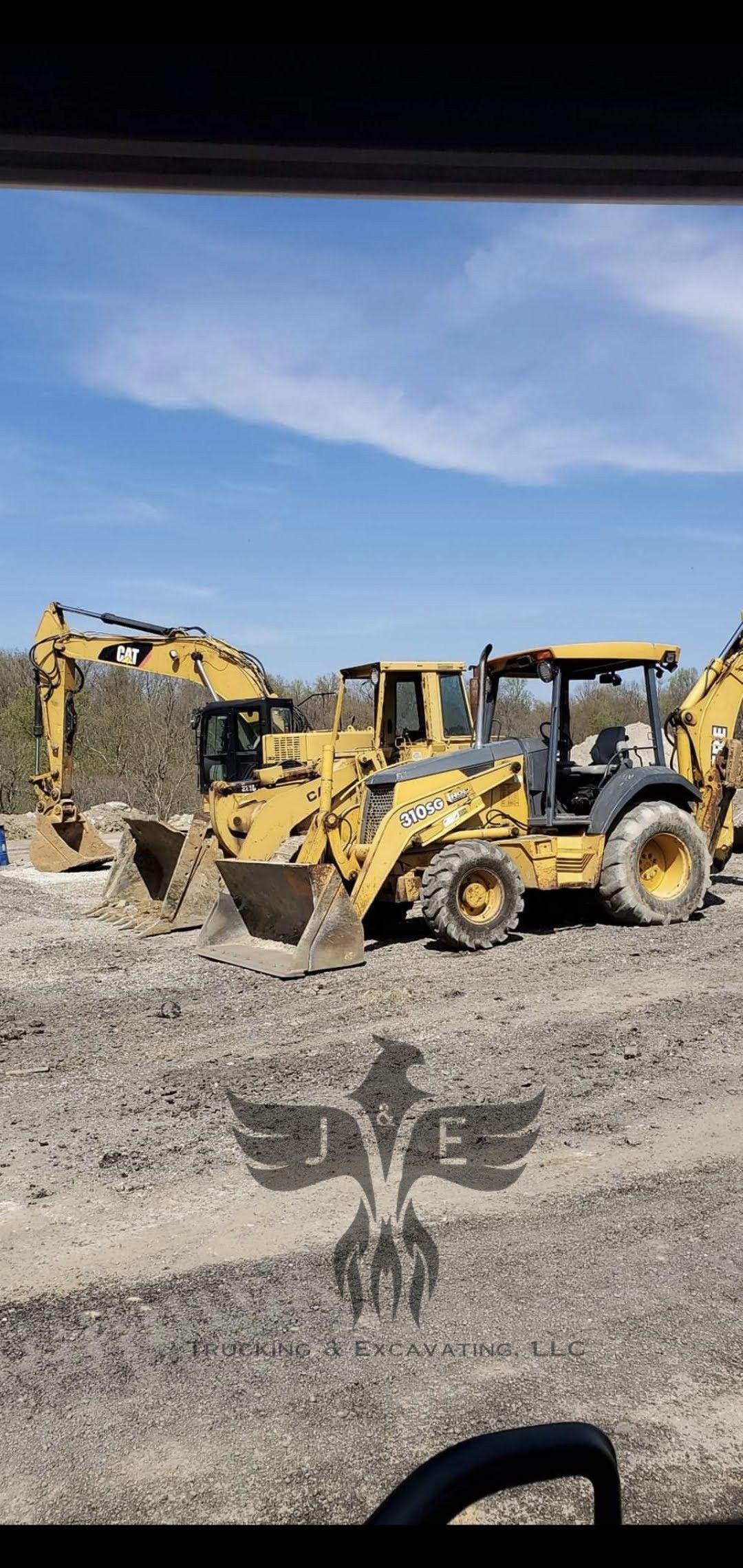 Two yellow excavators on a gravel construction site under a blue sky.