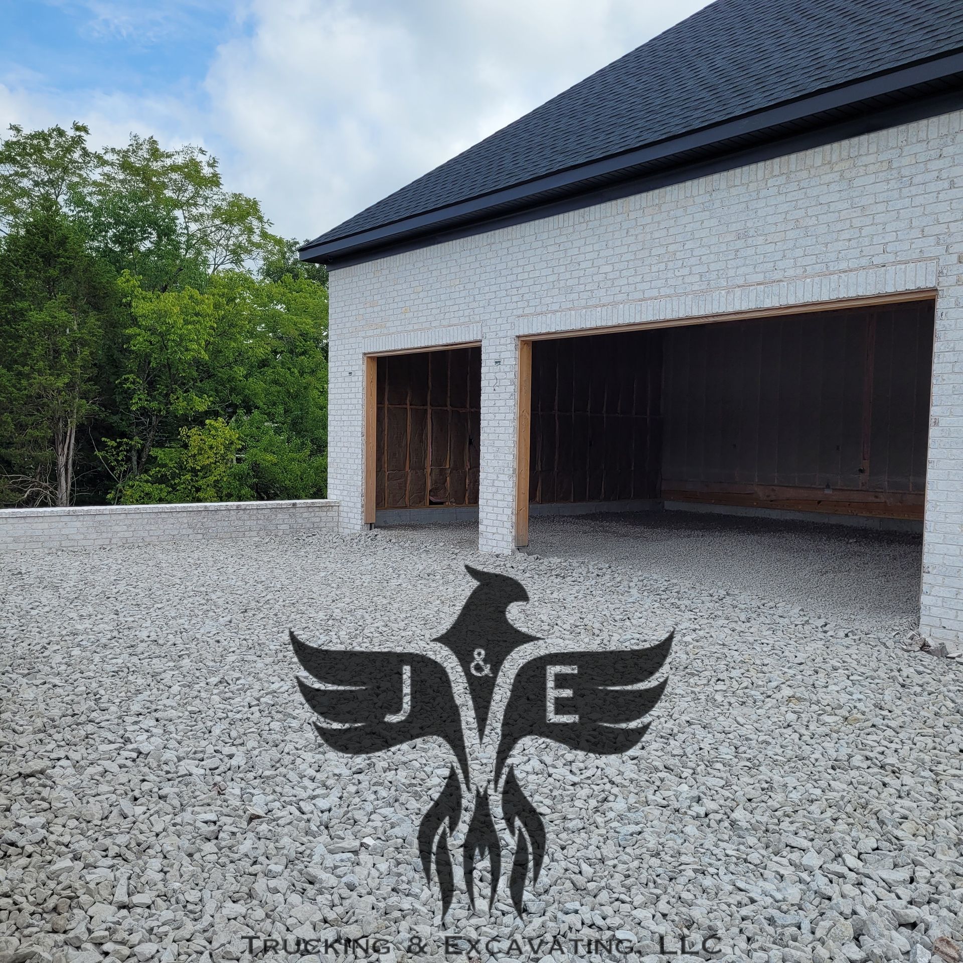 Gray gravel driveway beside a white garage with dark roof, framed by green trees.