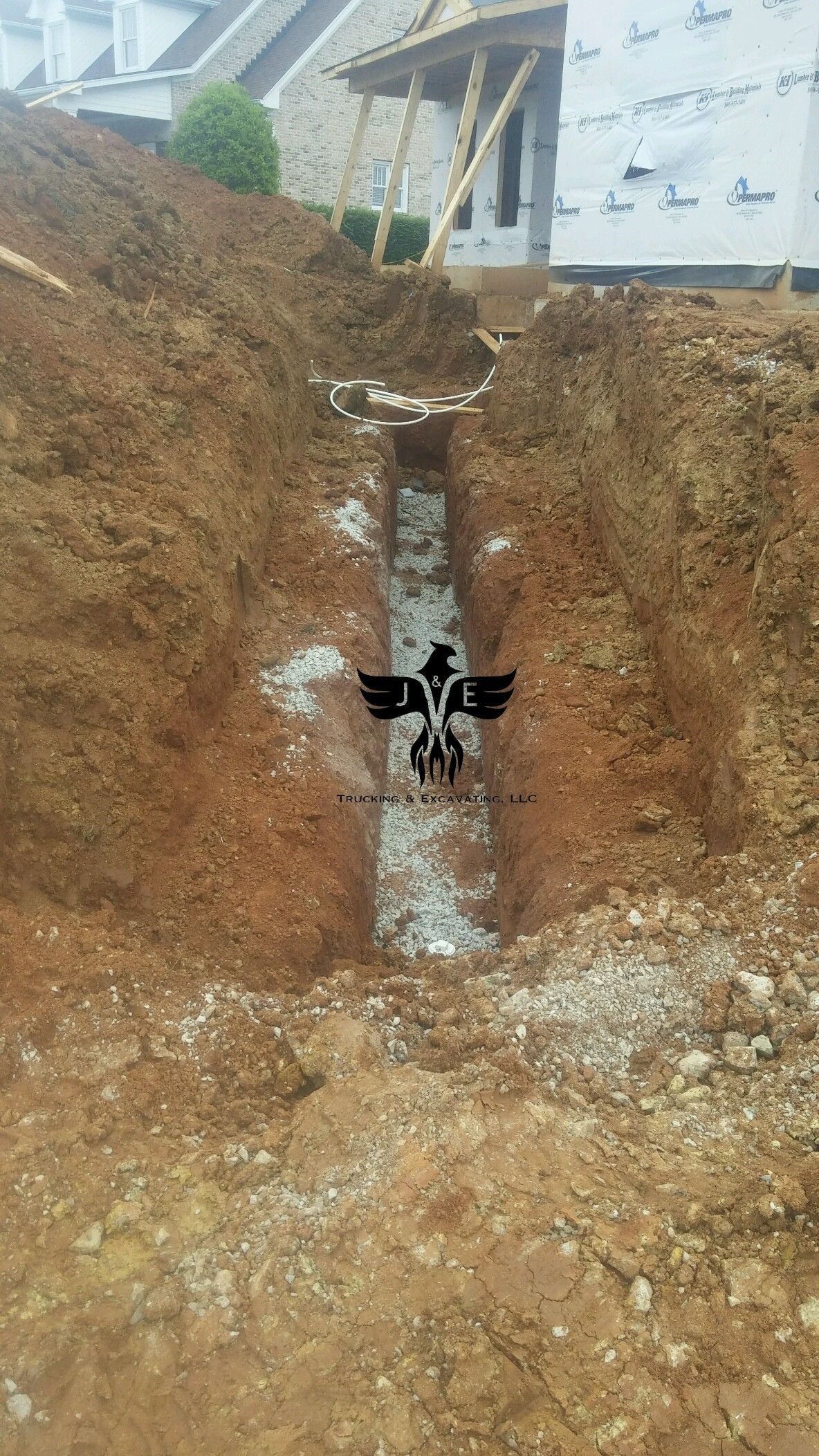 Excavated trench with exposed soil and a narrow concrete drain beneath a building under construction