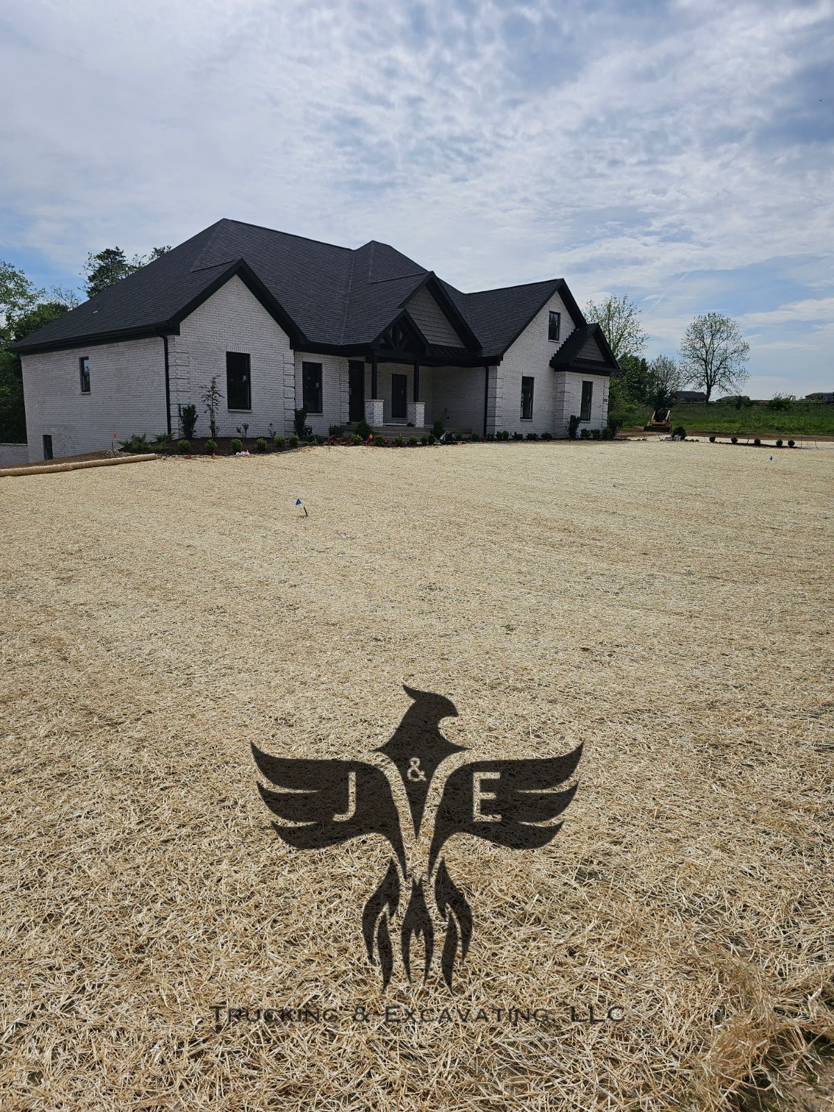 Modern house with dark roof behind a gravel yard featuring a winged emblem.