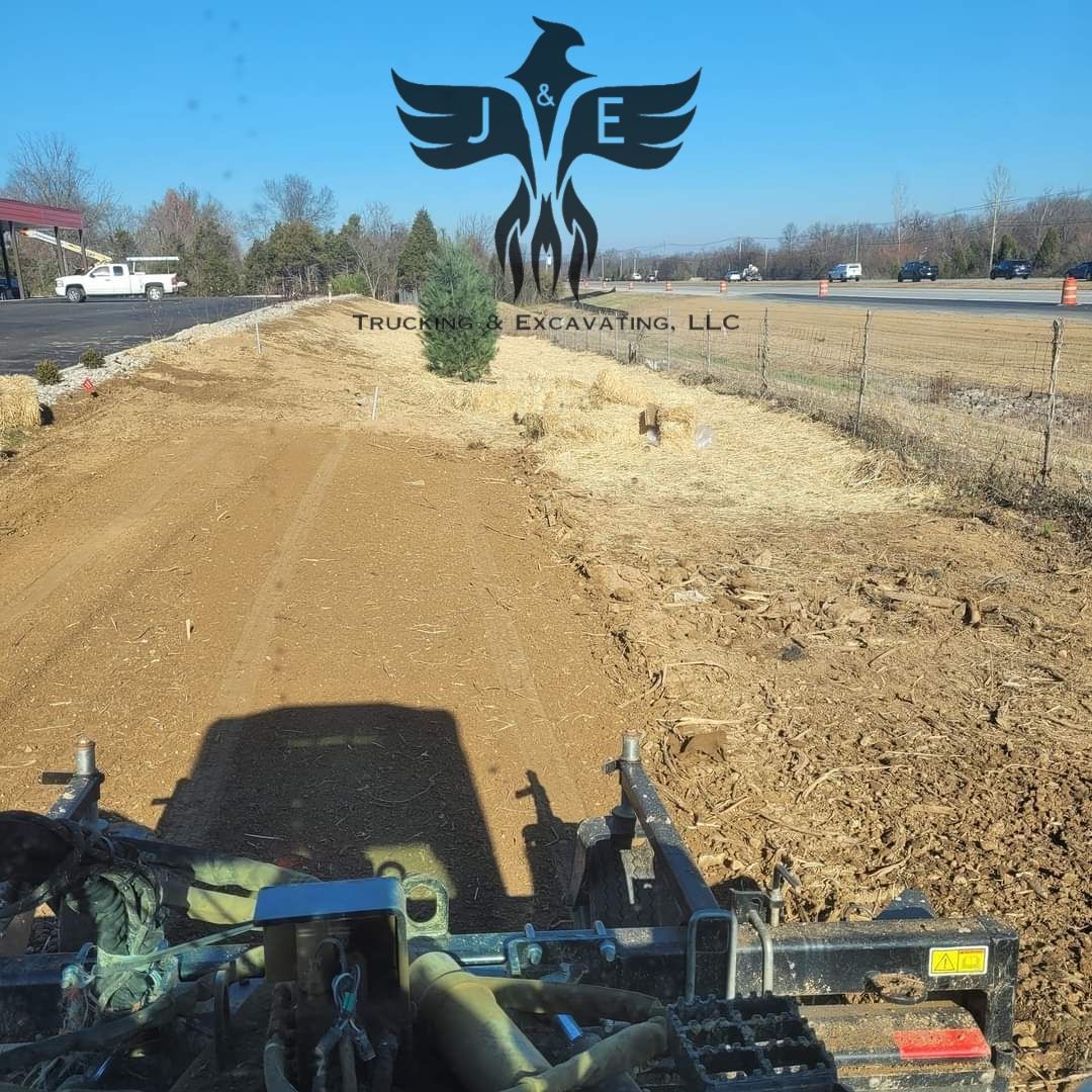 Skid-steer view of a dirt path with a winged metal sculpture and landscaped roadside ahead on a sunny day