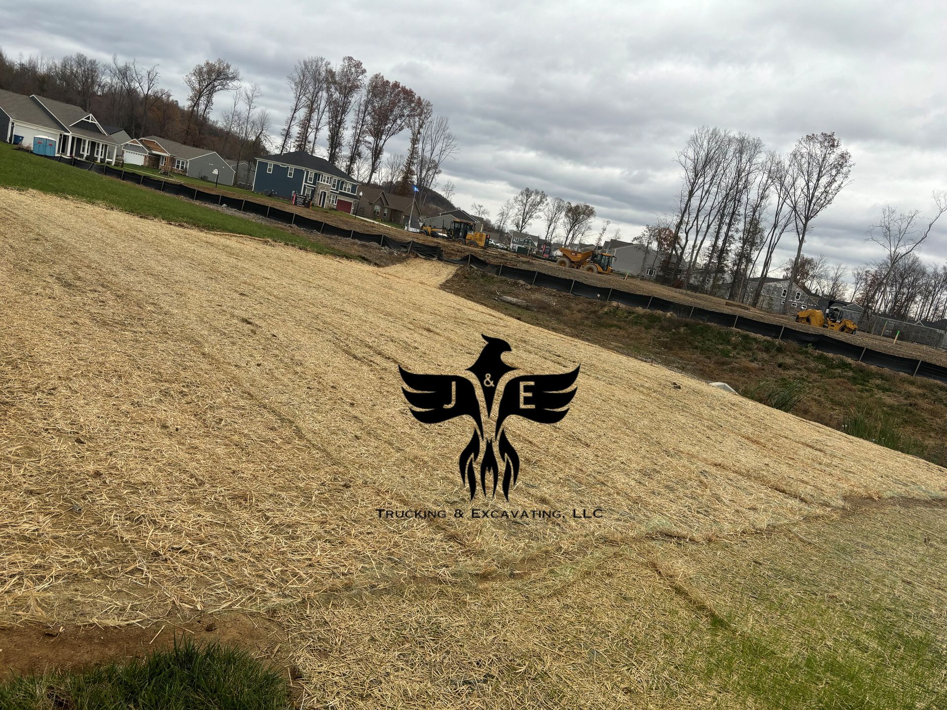 Farm field with a black bird logo centered on a sloped, harvested hillside under cloudy sky.