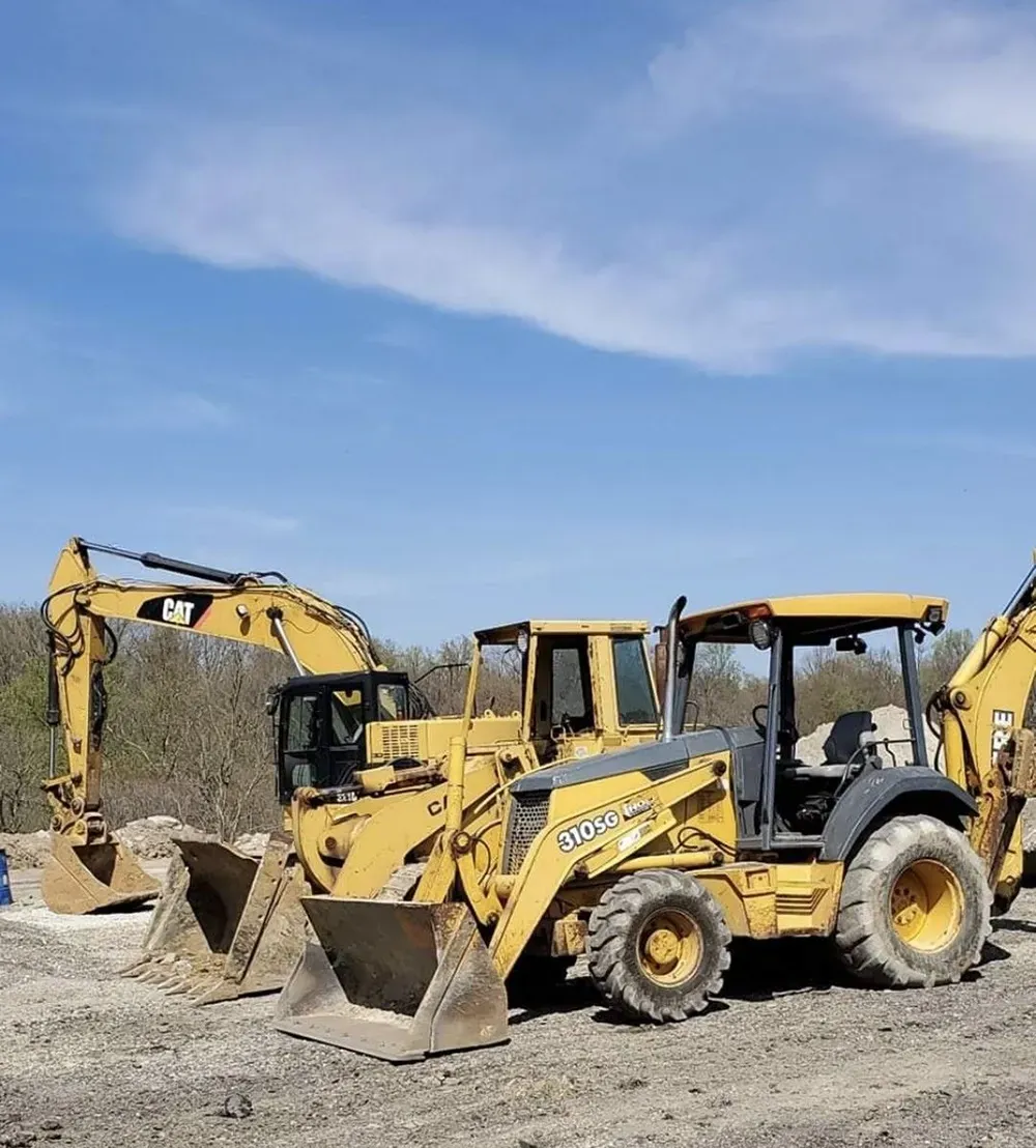 Yellow backhoe loaders and excavators parked on a gravel site under a blue sky.
