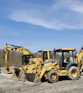 Yellow construction machinery parked on a gravel lot under a blue sky
