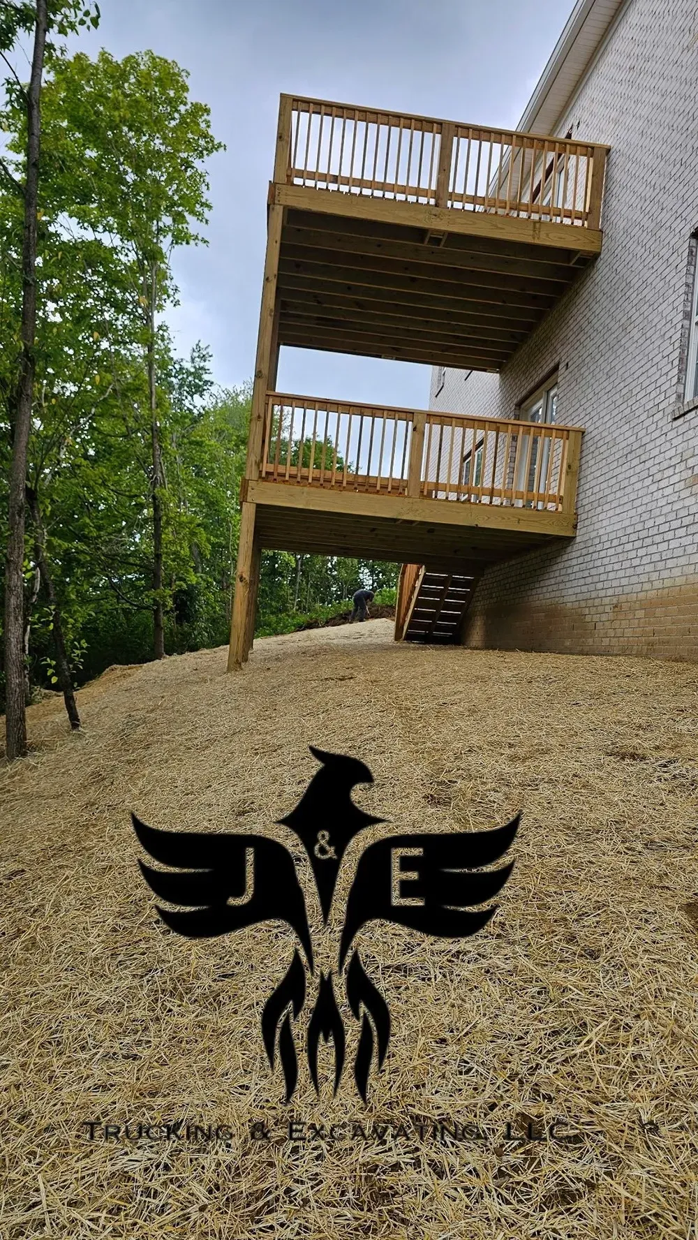 Wooden balconies on a white building beside trees and gravel, with a black bird logo in the foreground.