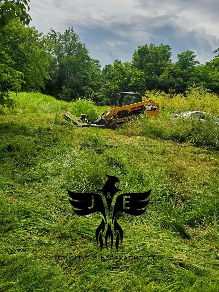 Yellow excavator in a green grassy field with trees in the background