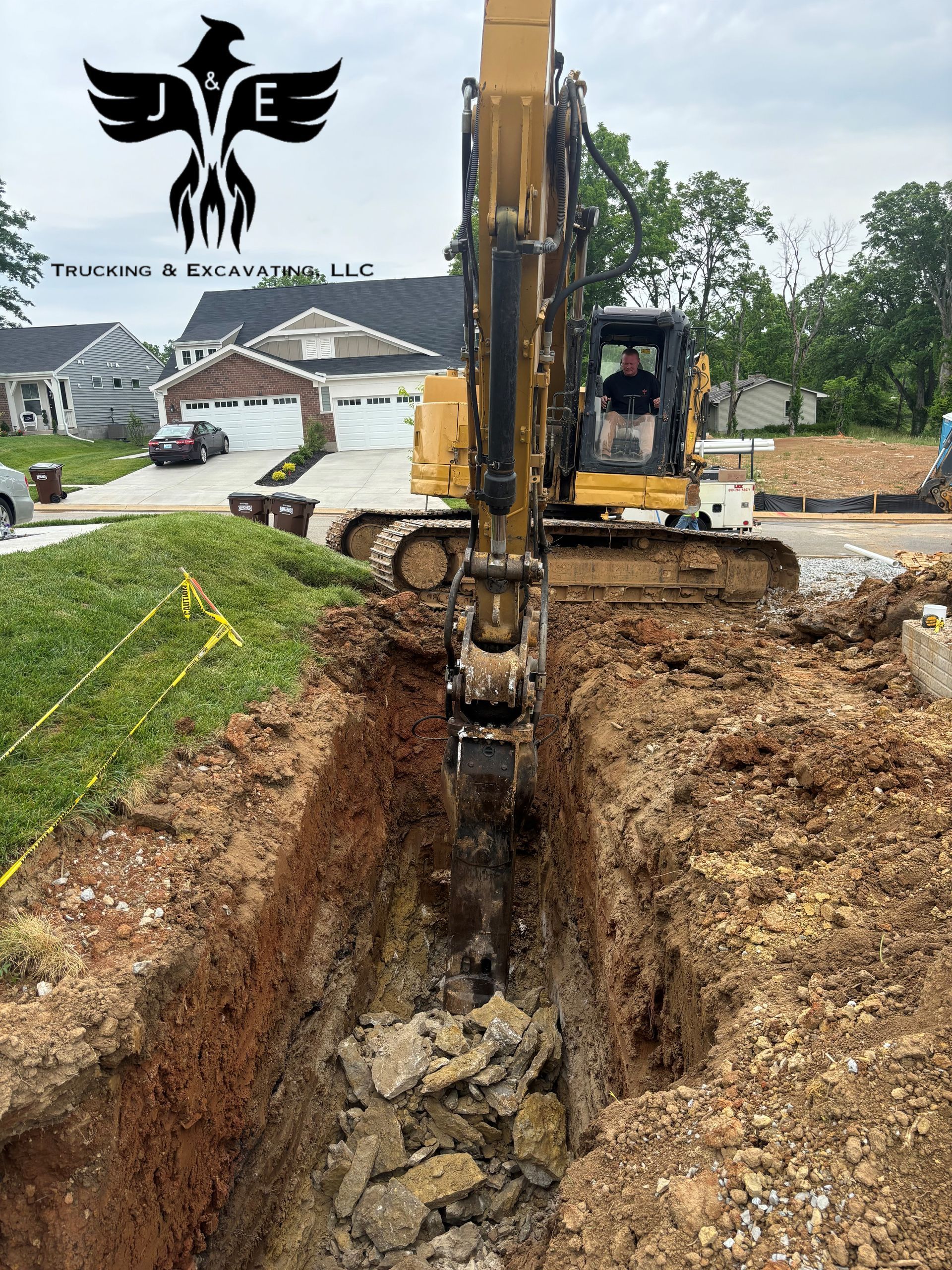 Excavator digging a deep trench in a residential construction site with dirt piles and houses nearby
