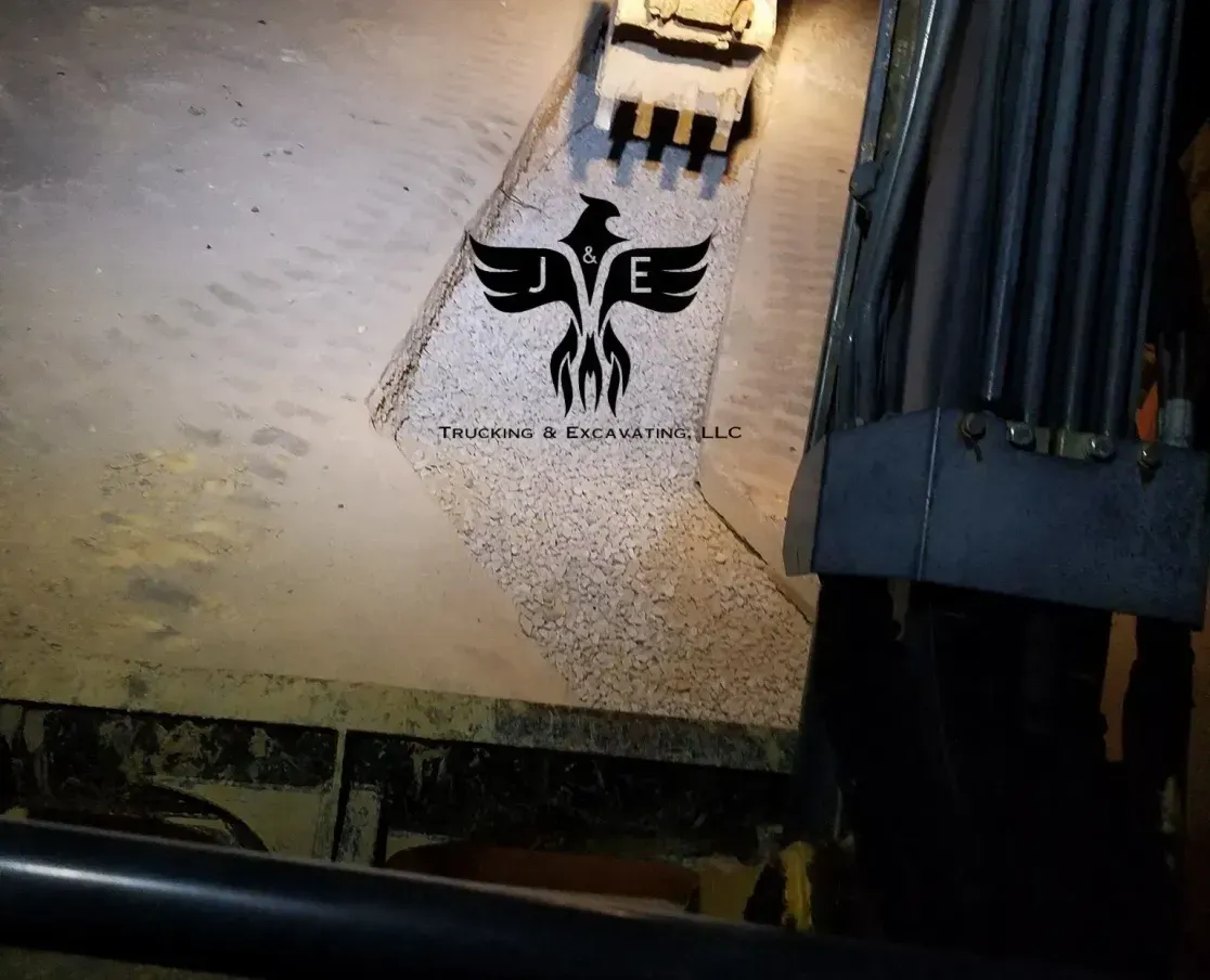 Nighttime view of a black eagle insignia painted on pavement beside a lit excavator arm and building edge