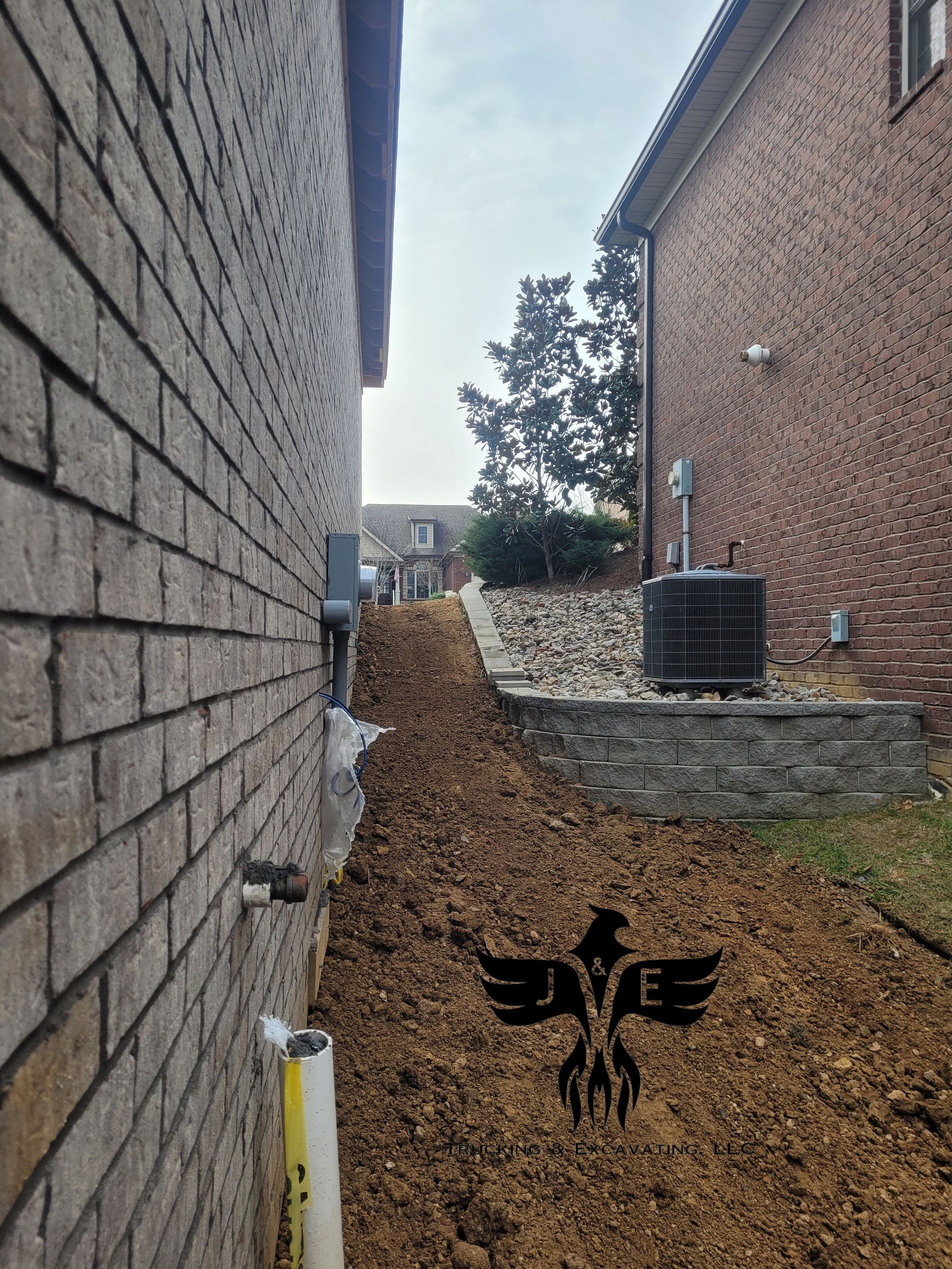 Narrow gravel alley between two brick walls with a black winged bird mural on the ground.