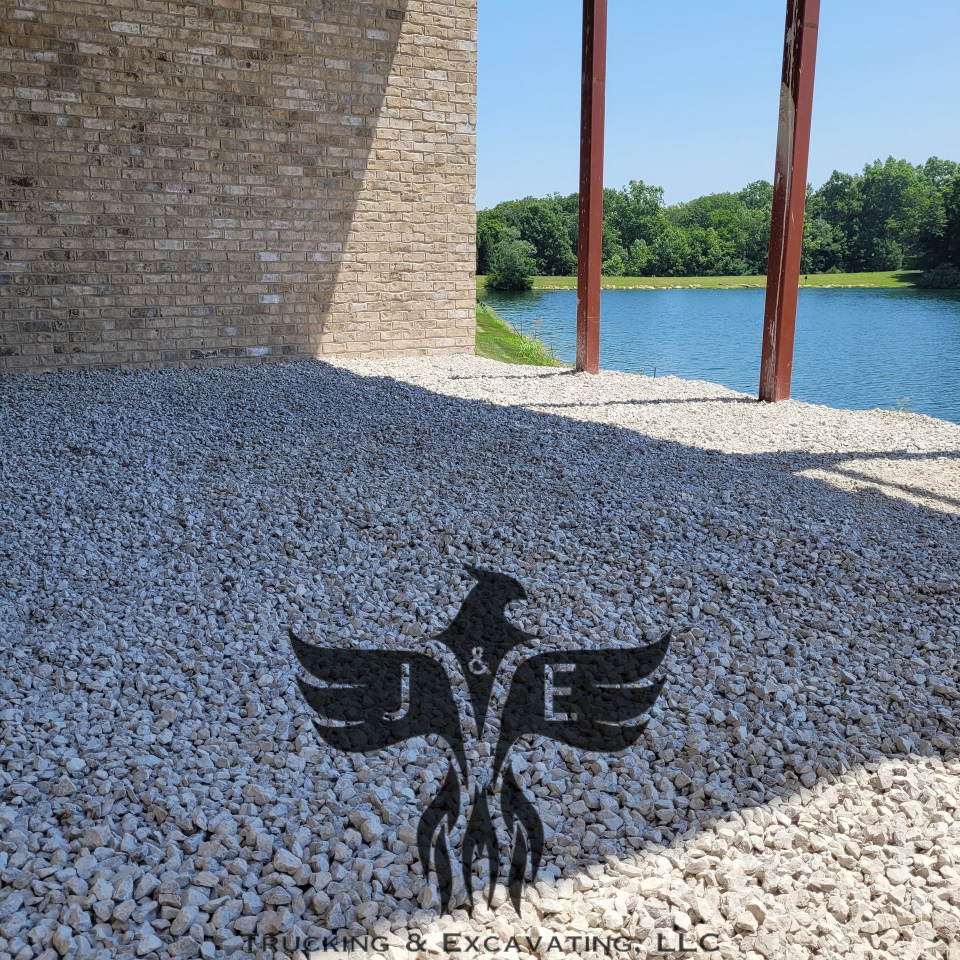Wings logo on white pebbles beside a stone wall, with water and trees in the background.