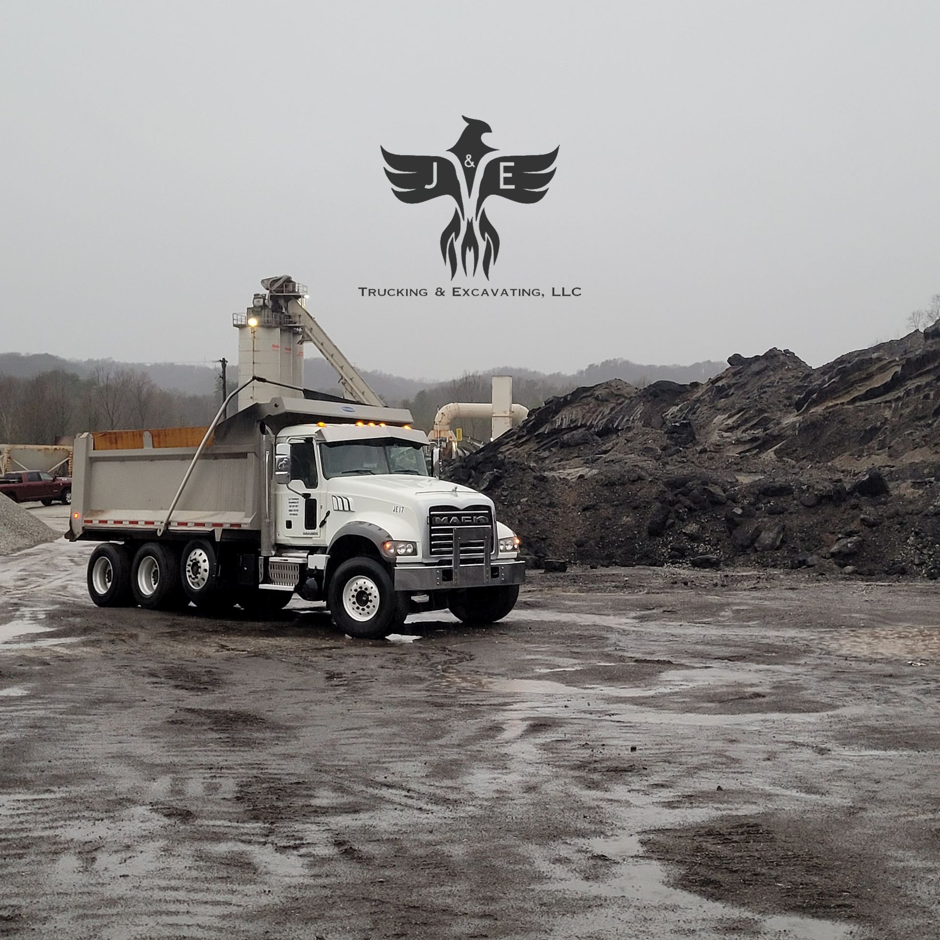 White dump truck at a muddy construction site beside a large dirt pile under a gray sky