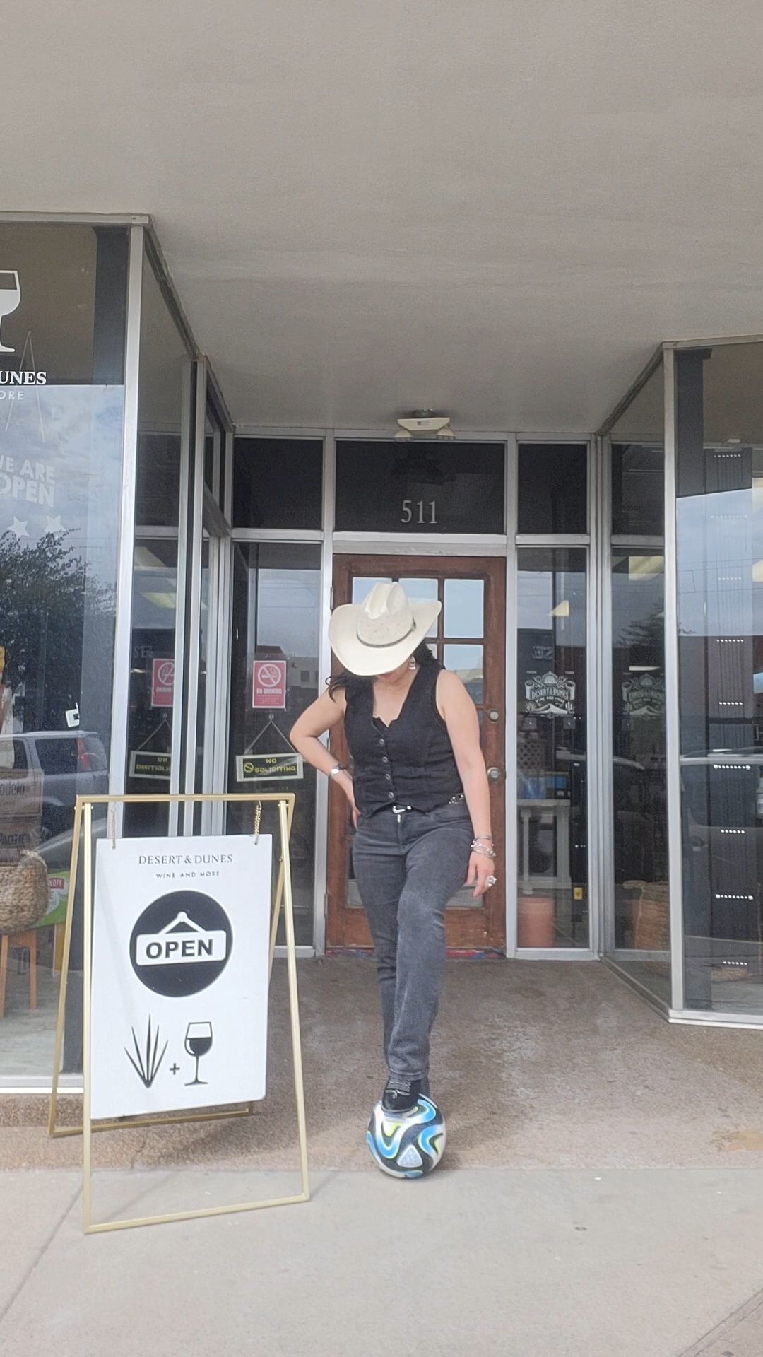 Person in a white hat stands at a storefront entrance, facing away, with a blue scooter on the ground.