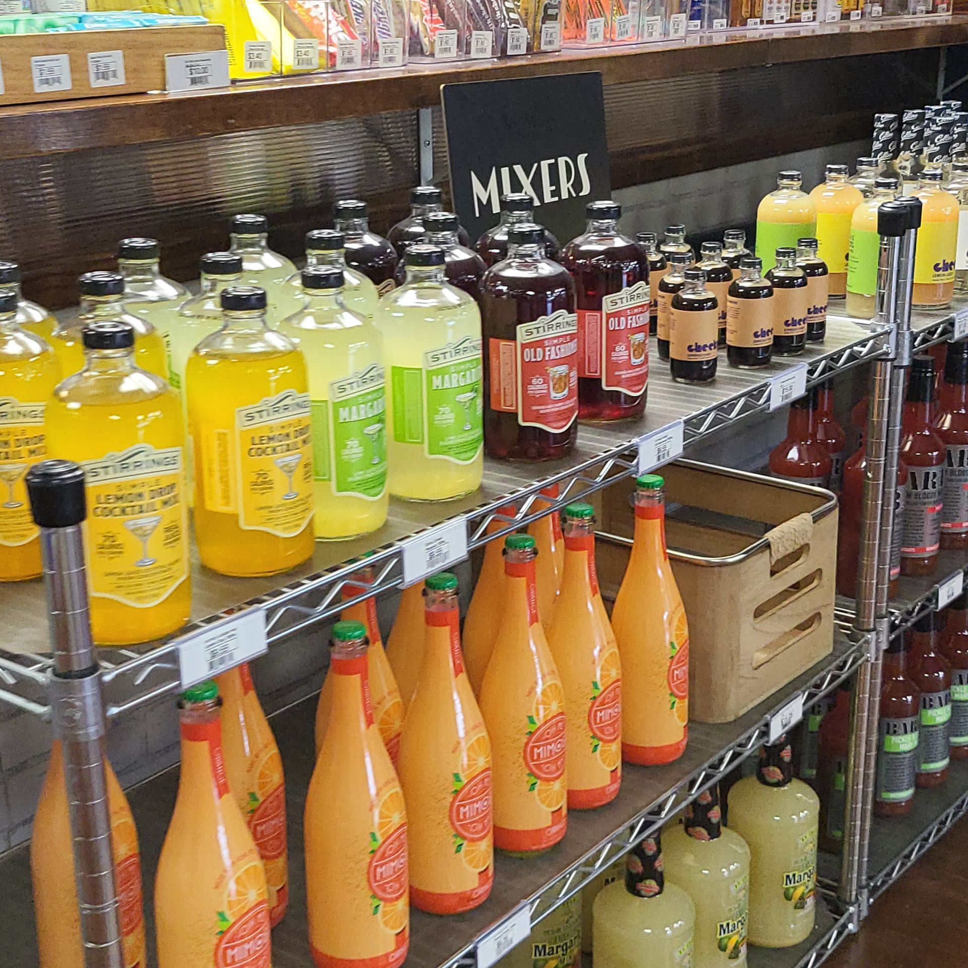 Store shelf stocked with assorted colorful bottled mixers and juices, labeled by flavor.