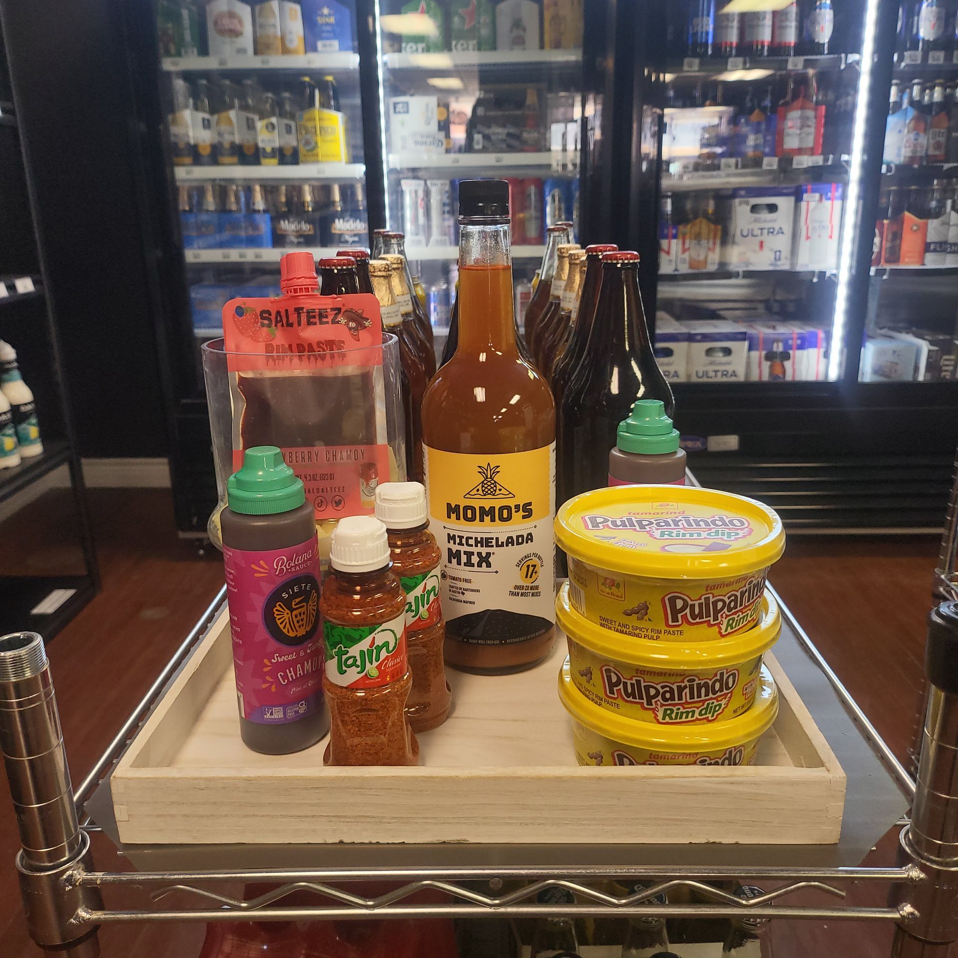 Assorted condiments and sauces on a wooden tray in a store cooler.