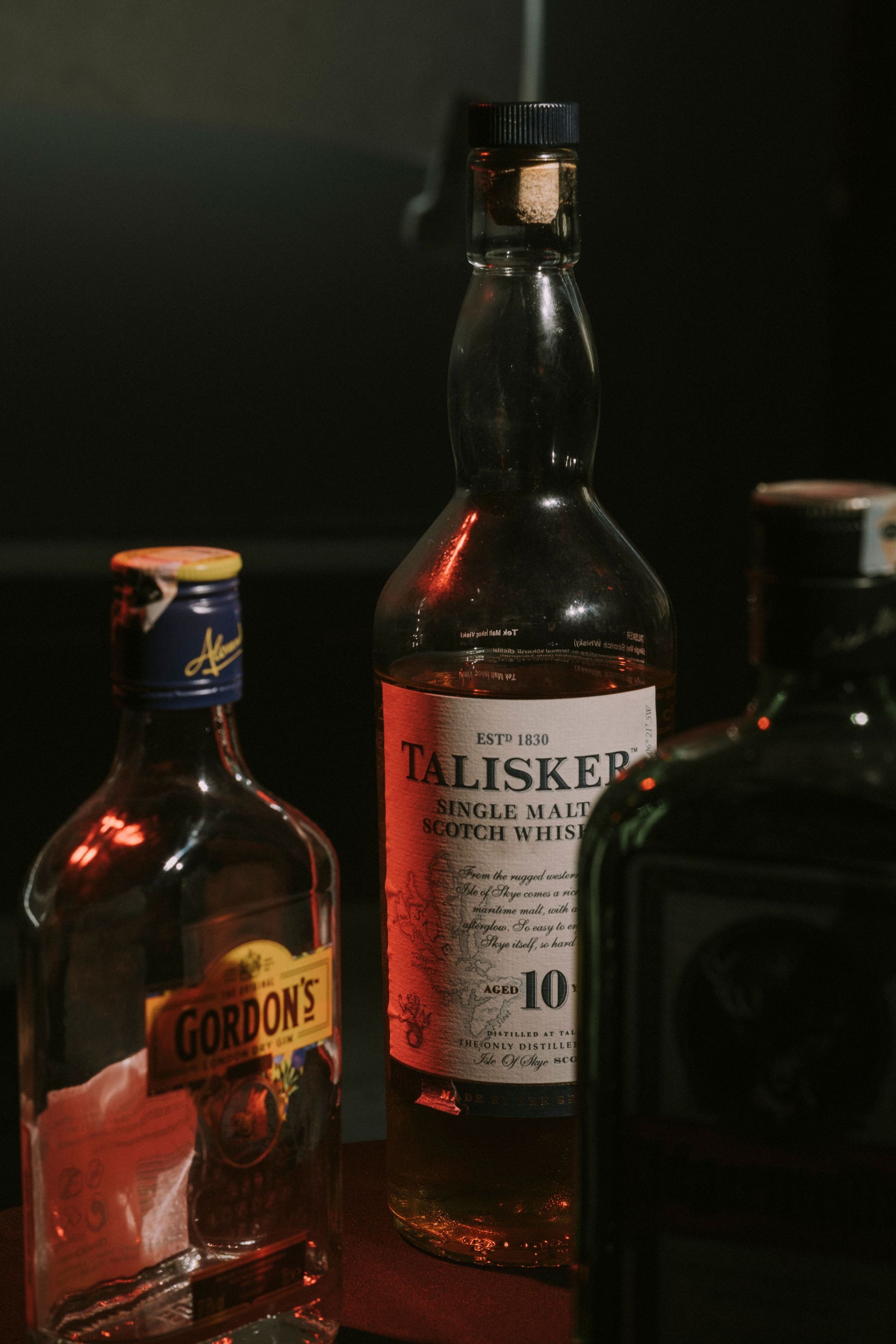 Three liquor bottles on a dark background, including a Talisker 10 bottle in the center.