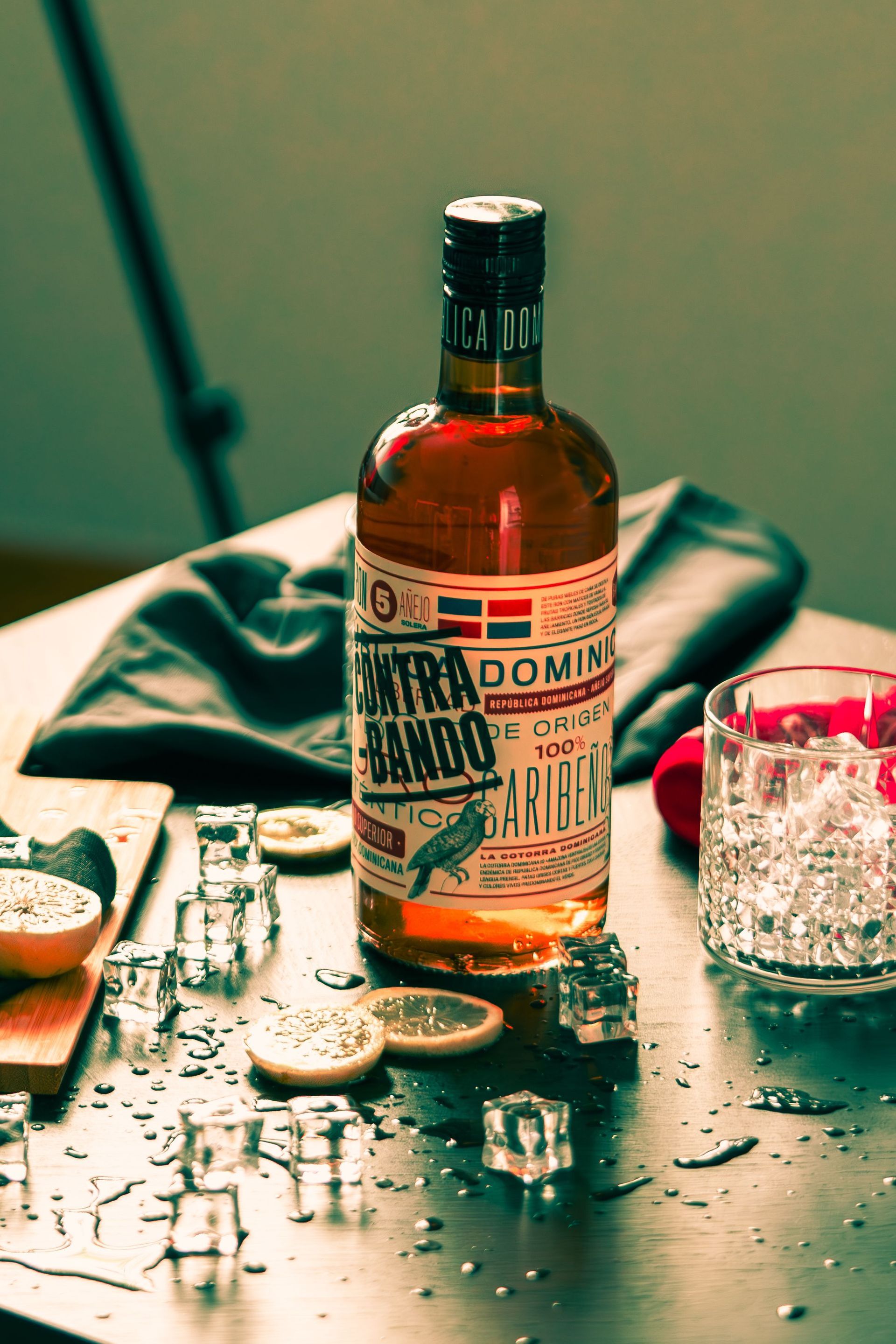 Bottle of bourbon on a table with a glass of ice, scattered ice cubes, and a lemon wedge