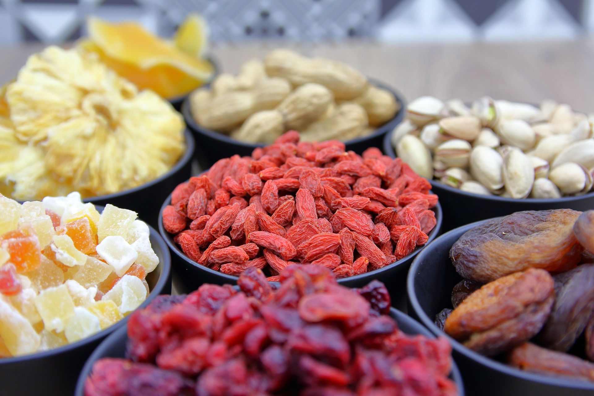 Assorted dried fruits and nuts in bowls, including red goji berries, apricots, pistachios, and dates.