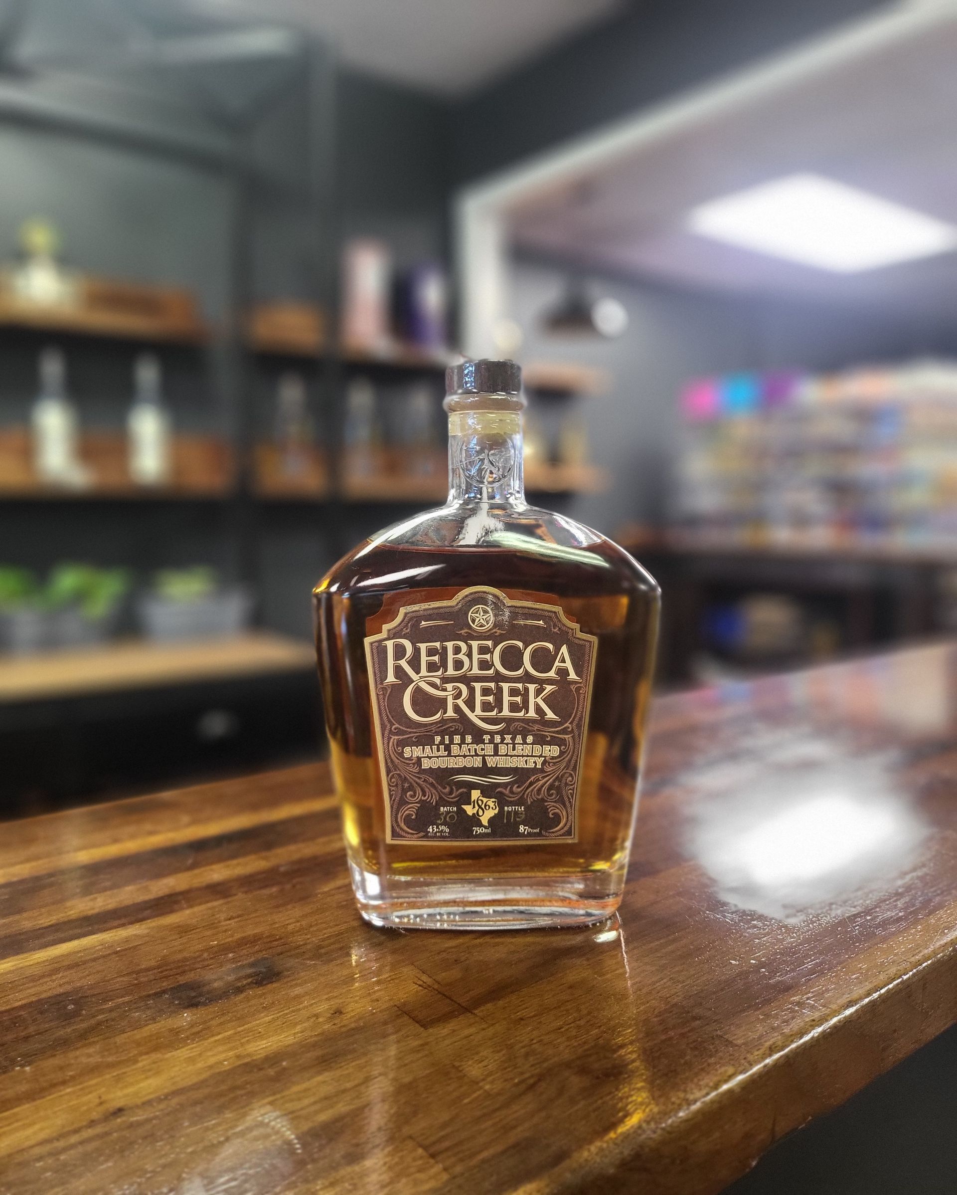 Rebel Creek liquor bottle on a wooden bar, with blurred shelves in the background