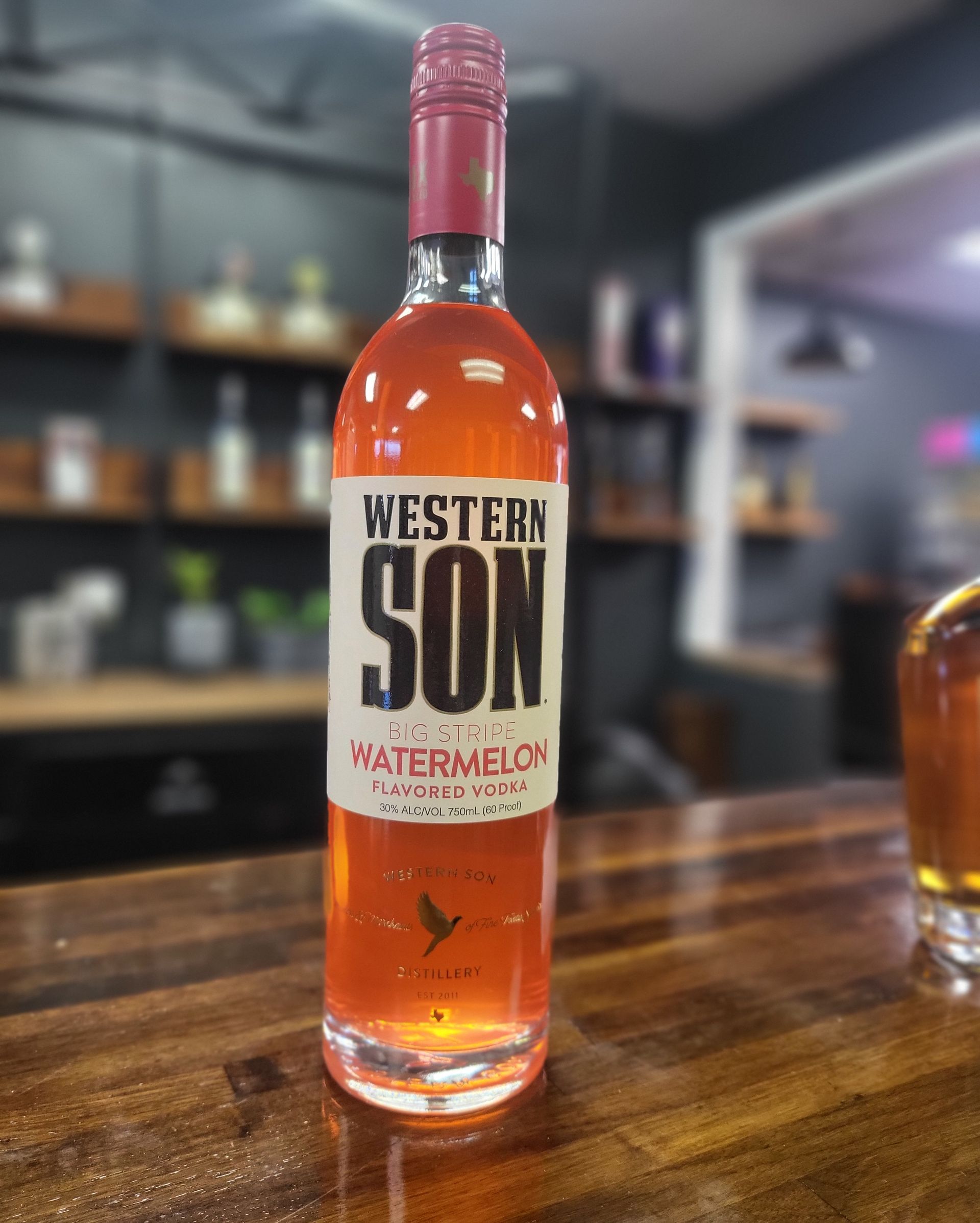 Bottle of Western Son watermelon vodka on a bar counter with a blurred liquor shelf background