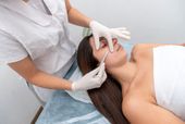 Person receiving facial injection from a medical professional. Clinic setting, white gloves, syringe.