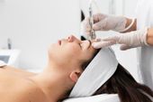 Person receiving a facial treatment with a handheld device, in a clinic setting.