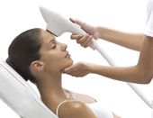 Woman receiving facial treatment with a handheld device on her forehead.