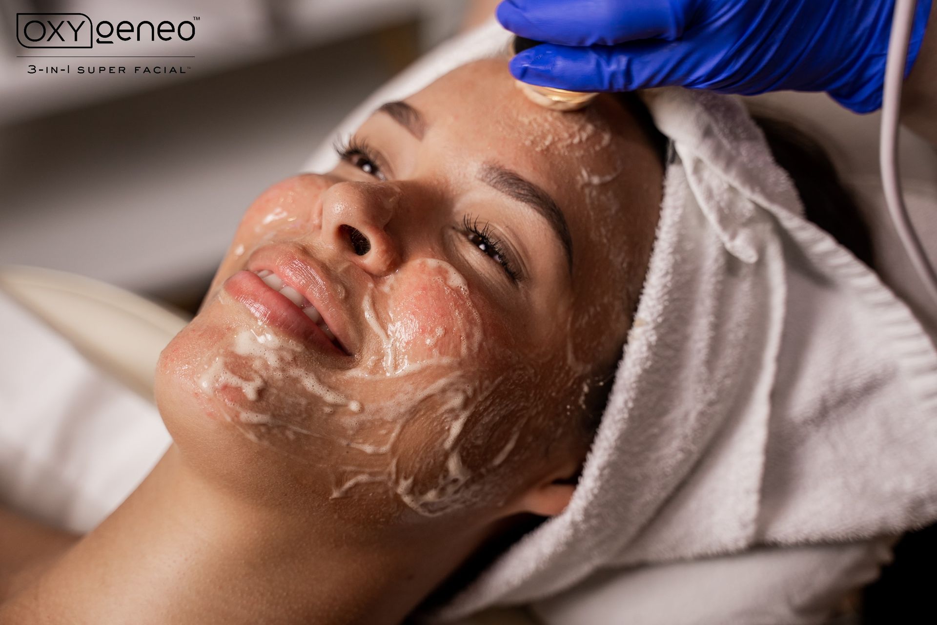 Woman receiving a facial treatment; cream on face, a gloved hand uses a device.