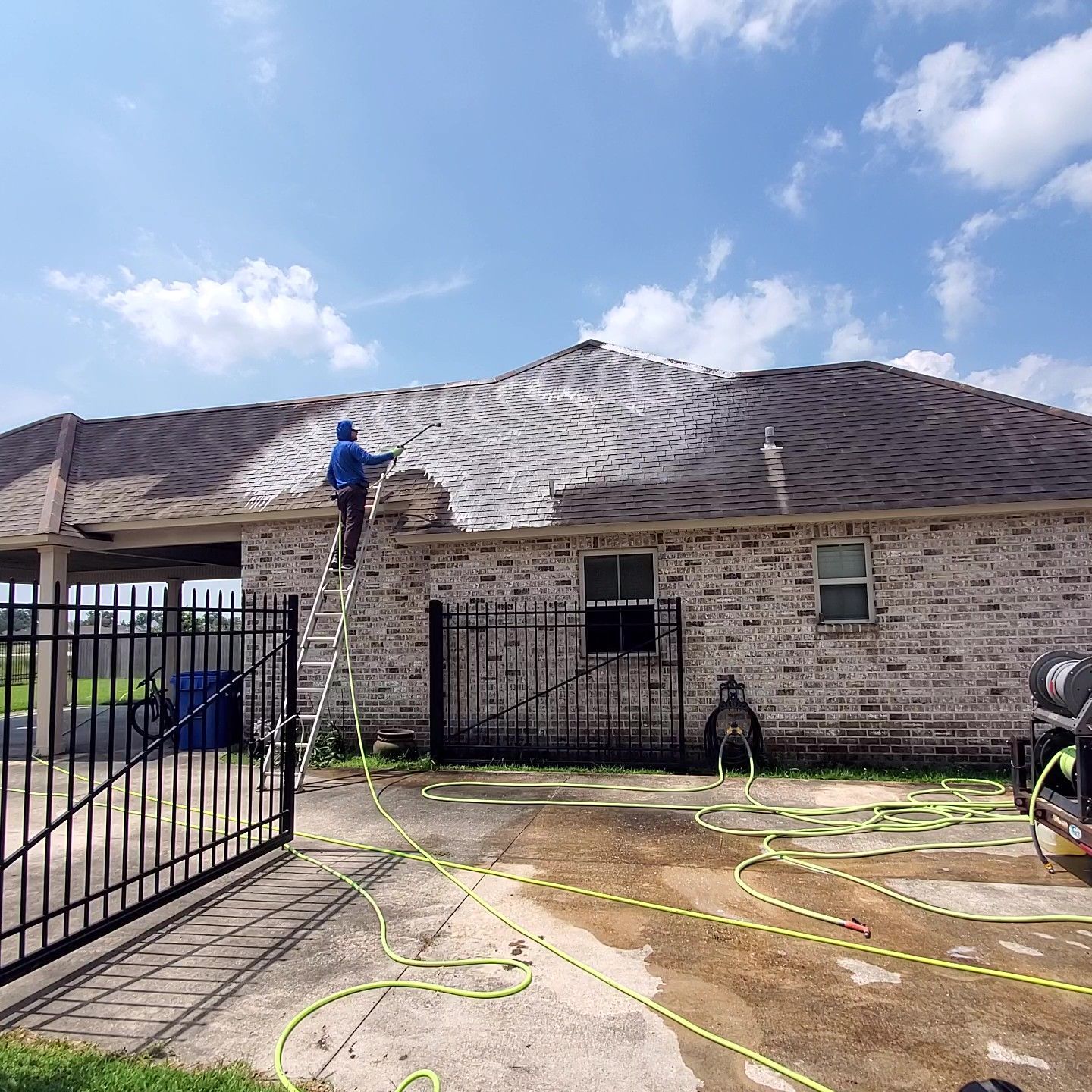 Person spraying water at a brick house with an American flag and front porch during cleanup