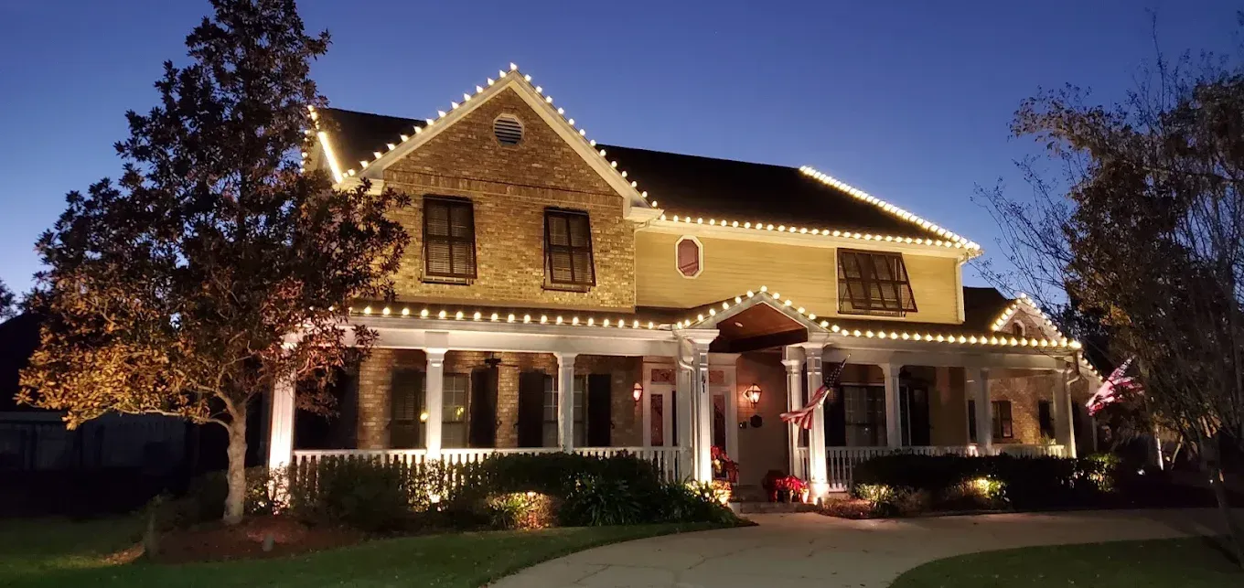 A warmly lit Victorian house at dusk, with string lights and a festive front porch.