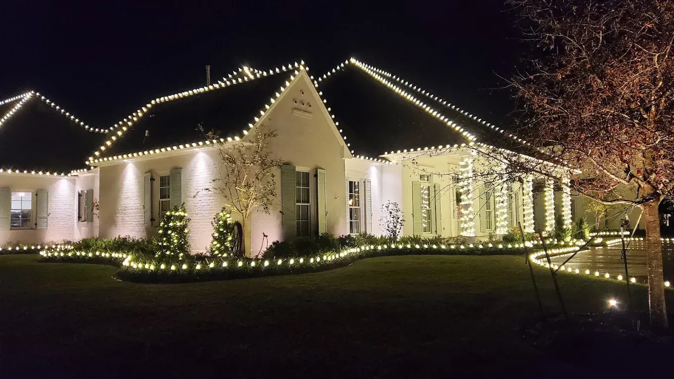 House at night outlined with white holiday lights and a lit walkway, with trees glowing in the yard