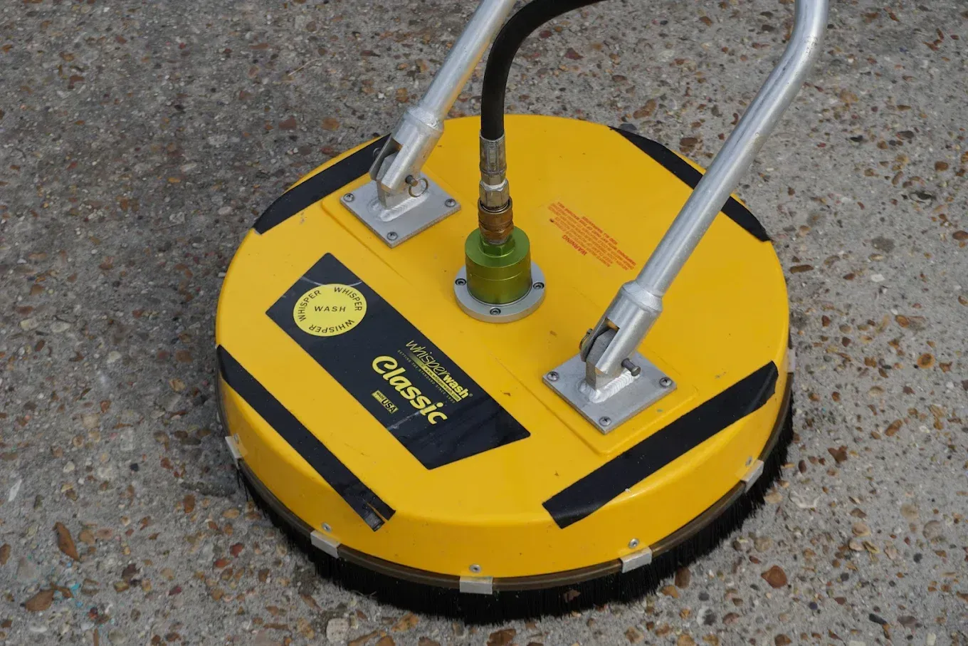 Yellow pavement-cleaning machine with metal handles on rough concrete surface