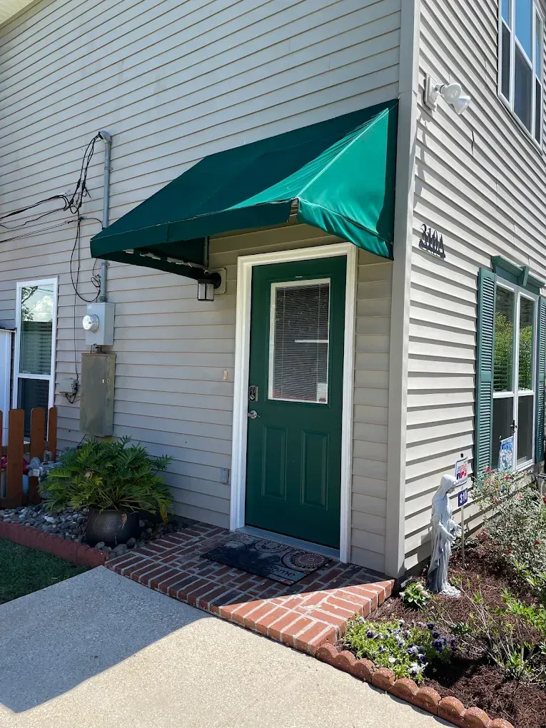 Green awning over a green door on a beige building exterior with brick edging and windows