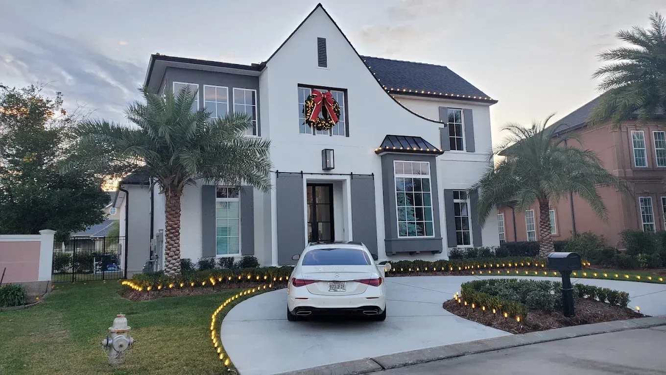 White two-story house with a wreath above the door, a parked white car, and a landscaped front yard at dusk