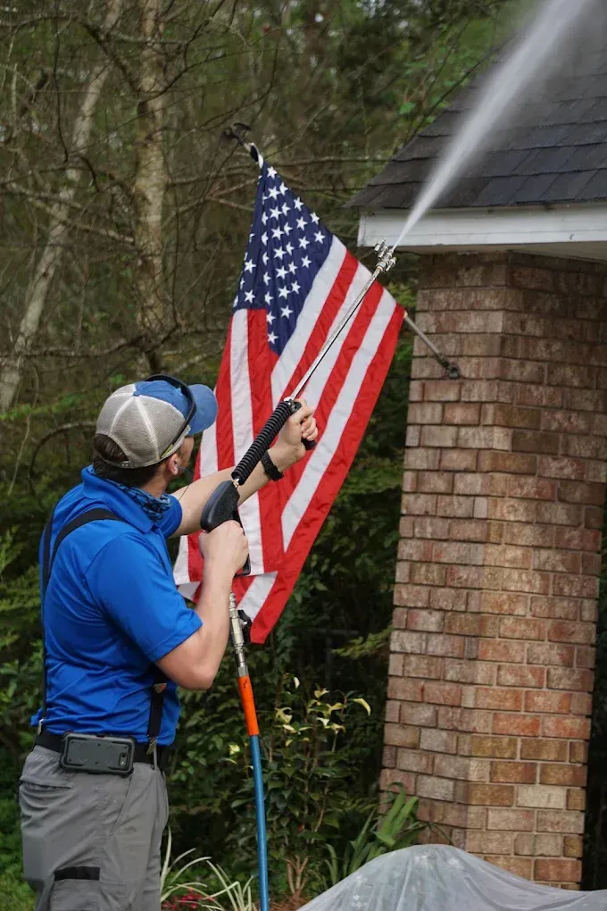 Person spraying an American flag on a brick house exterior with a pressure washer