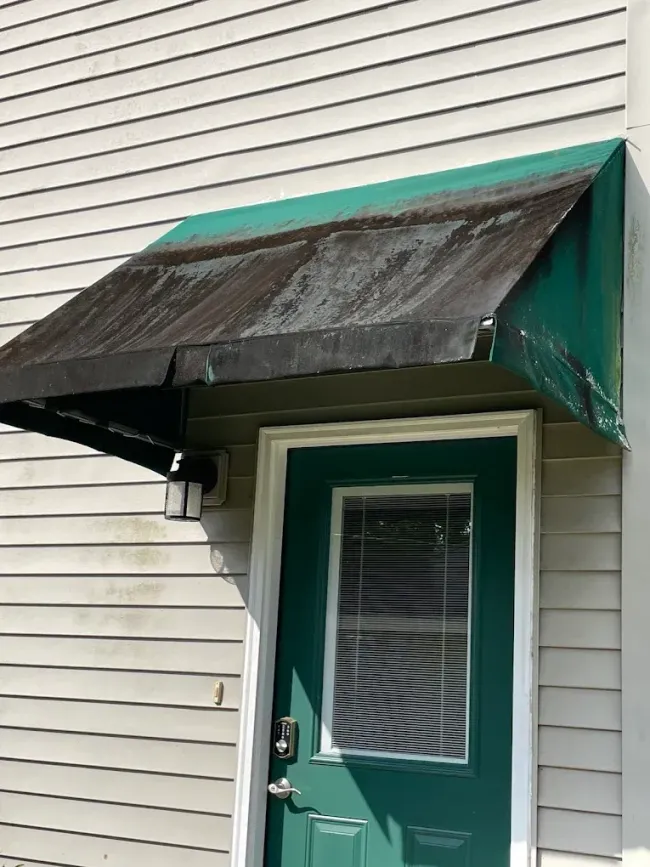 Green door under a worn dark awning on a house with white siding