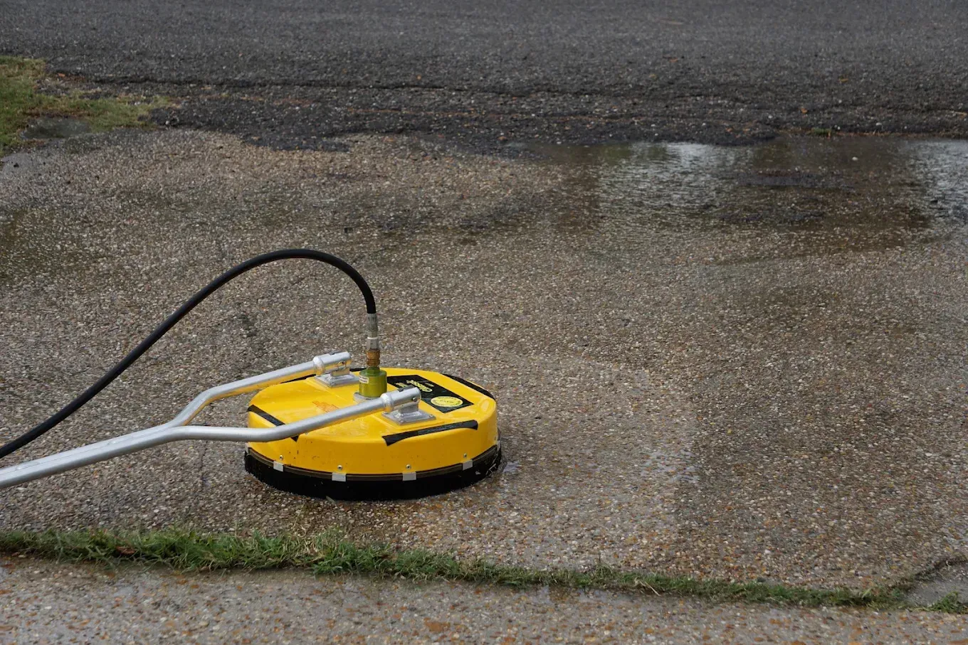 Yellow pressure washer on wet concrete, with hoses attached and water spraying the pavement.